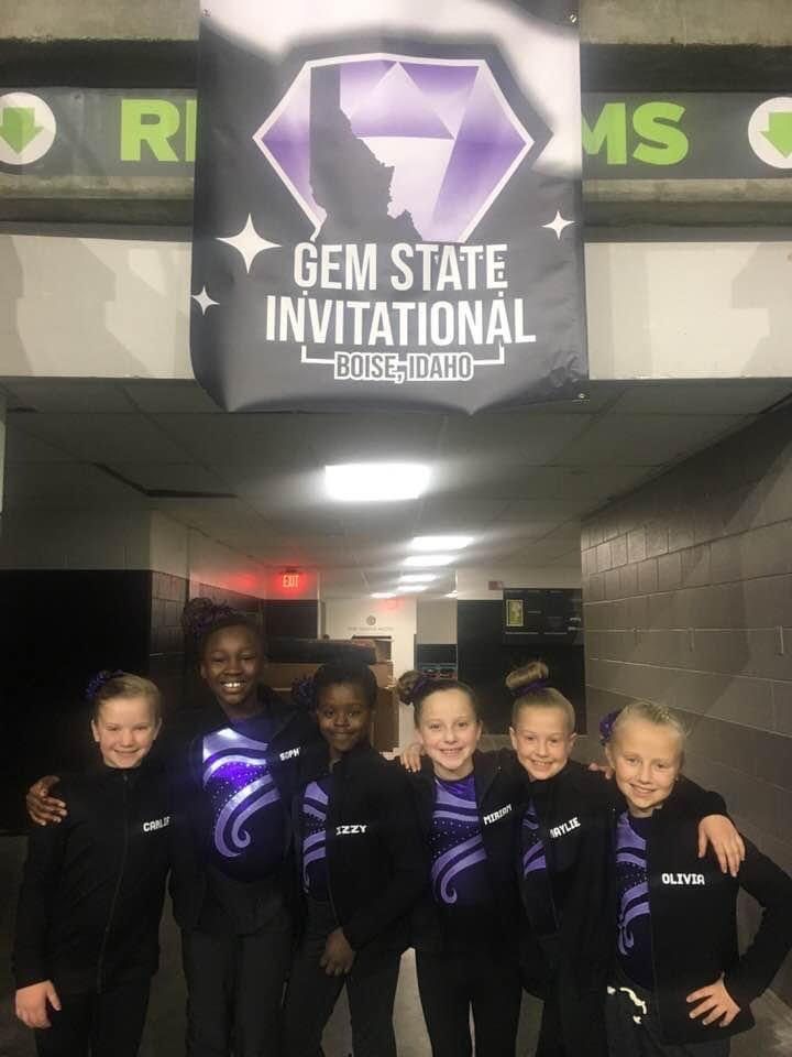 Six girls in matching purple team jackets posing under a Gem State Invitational banner.