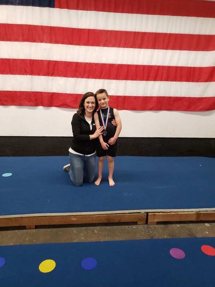 A coach kneeling beside a young boy with a medal in front of an American flag.