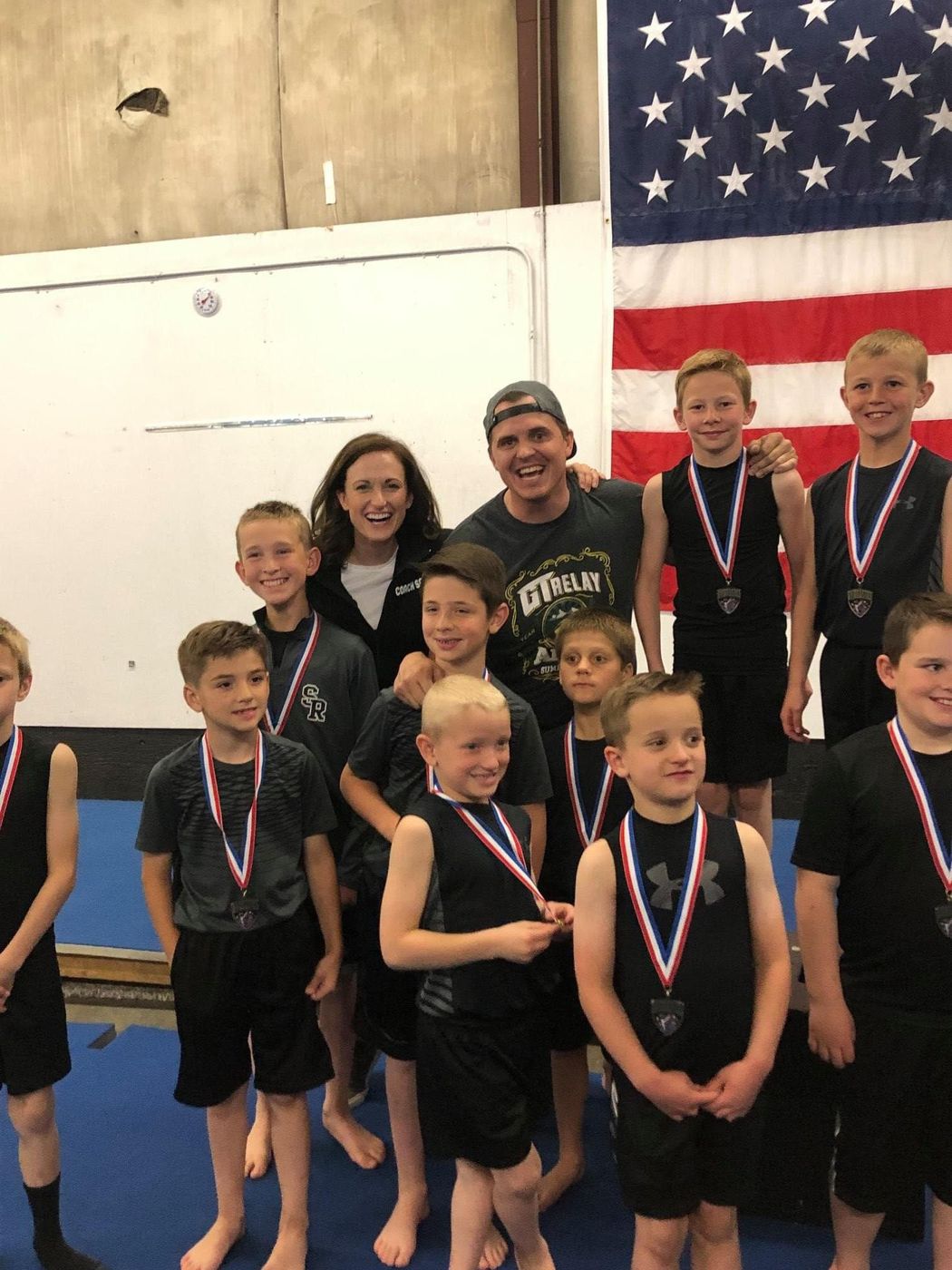 Two coaches posing with a group of boys wearing medals at a competition.