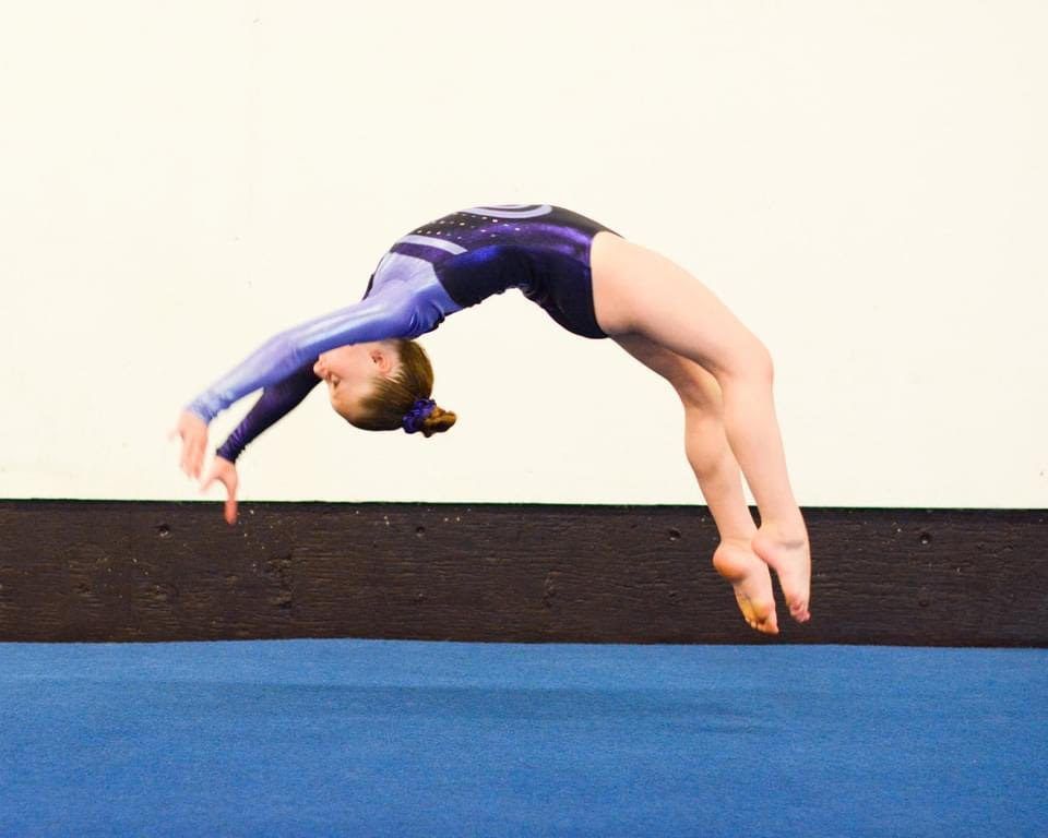 A gymnast performing a back handspring over the balance beam.