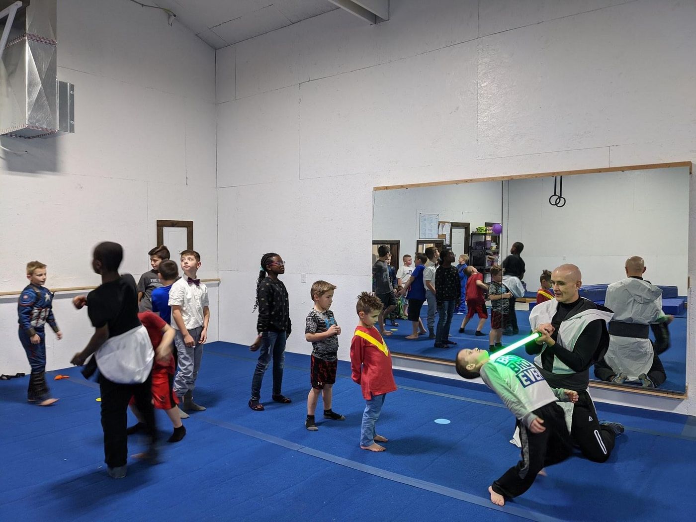 Children in costumes during a themed class in the gym, with a coach holding a foam saber.