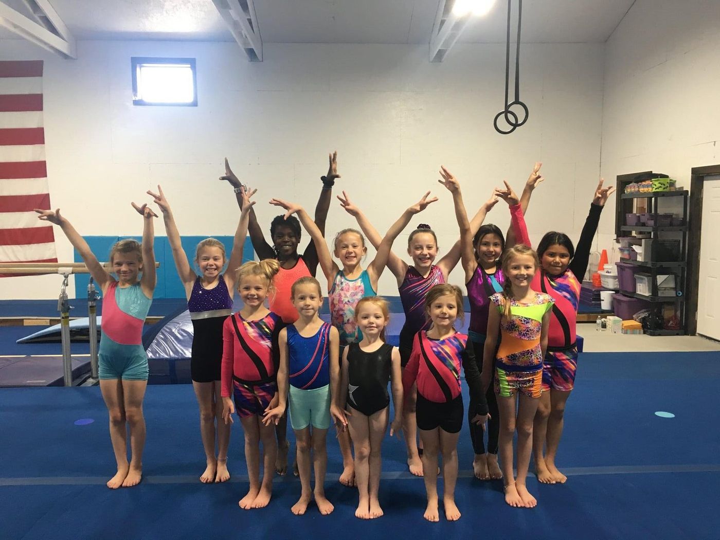 A large group of young gymnasts posing with arms raised in the gym.