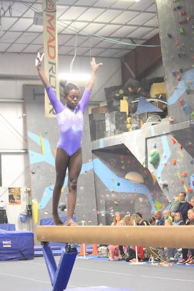 A young gymnast balancing on the beam with arms raised at a competition.