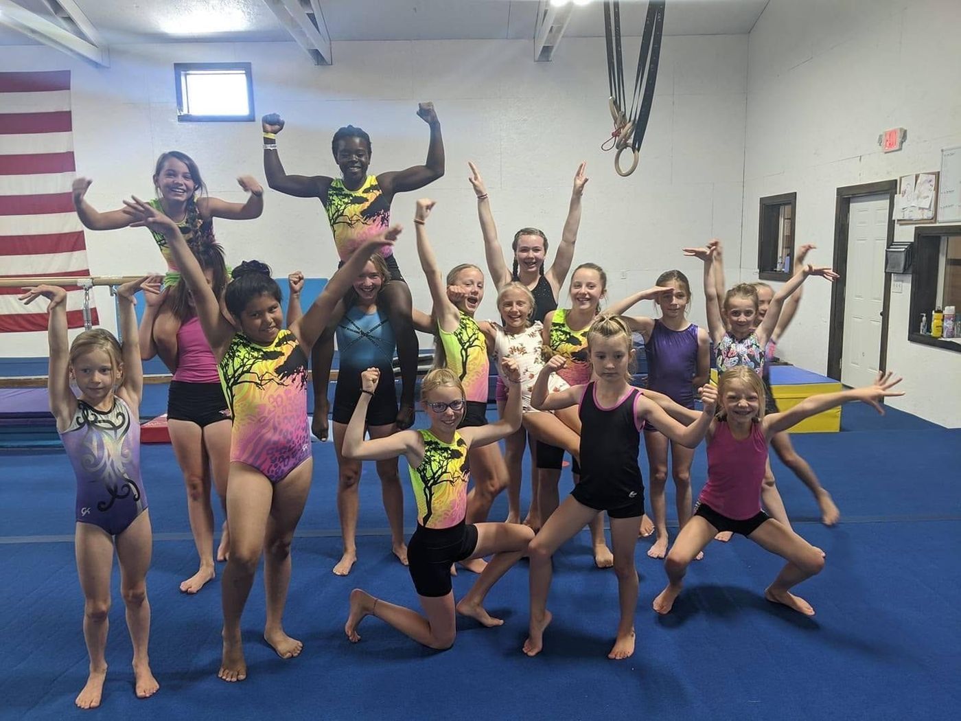 A large group of girls posing playfully with arms raised in the gym.