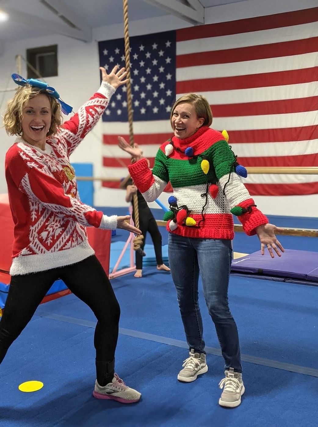 Two women in festive holiday sweaters posing playfully in the gym.