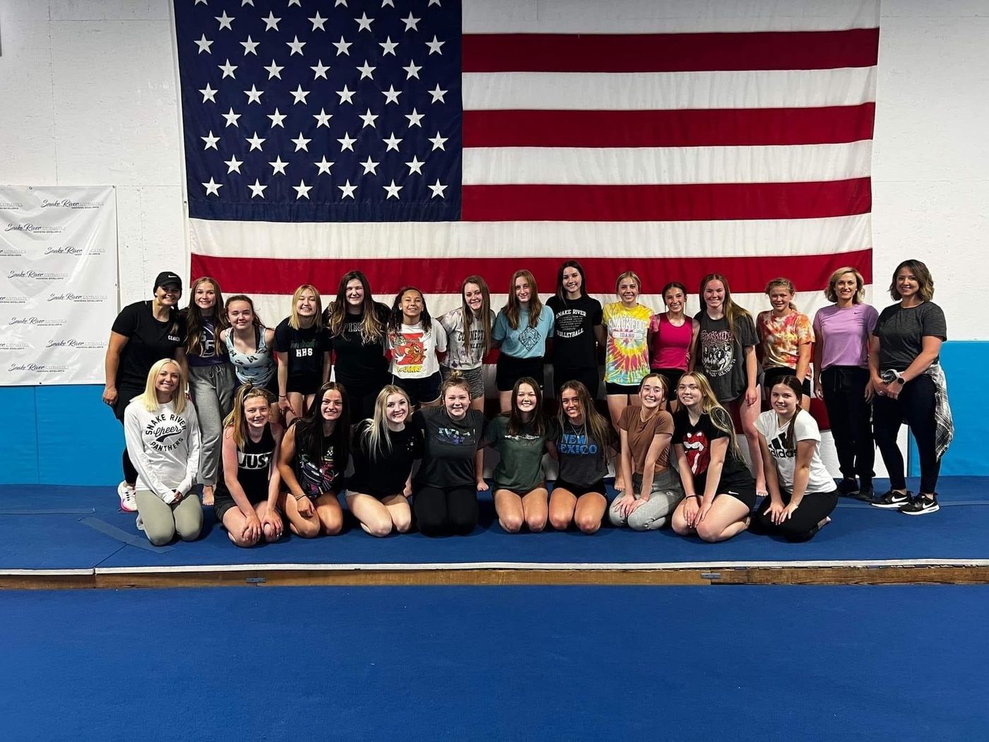 A group of teen gymnasts and coaches posing in front of an American flag.