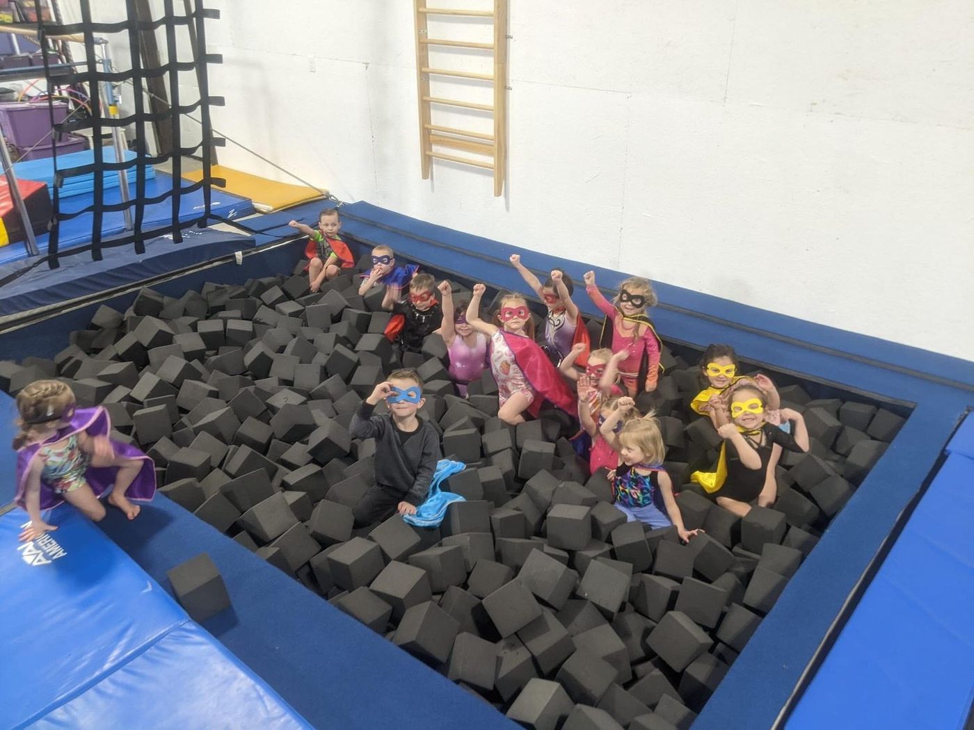 Young children in superhero costumes posing in a foam pit at the gym.