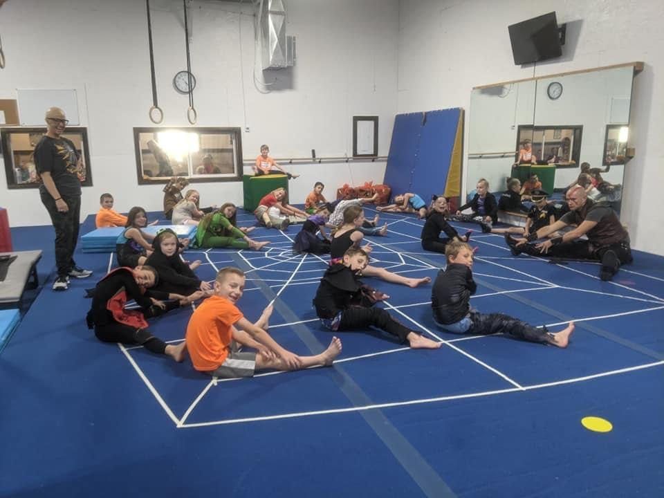Children in costumes stretching on the floor during a themed class in the gym.