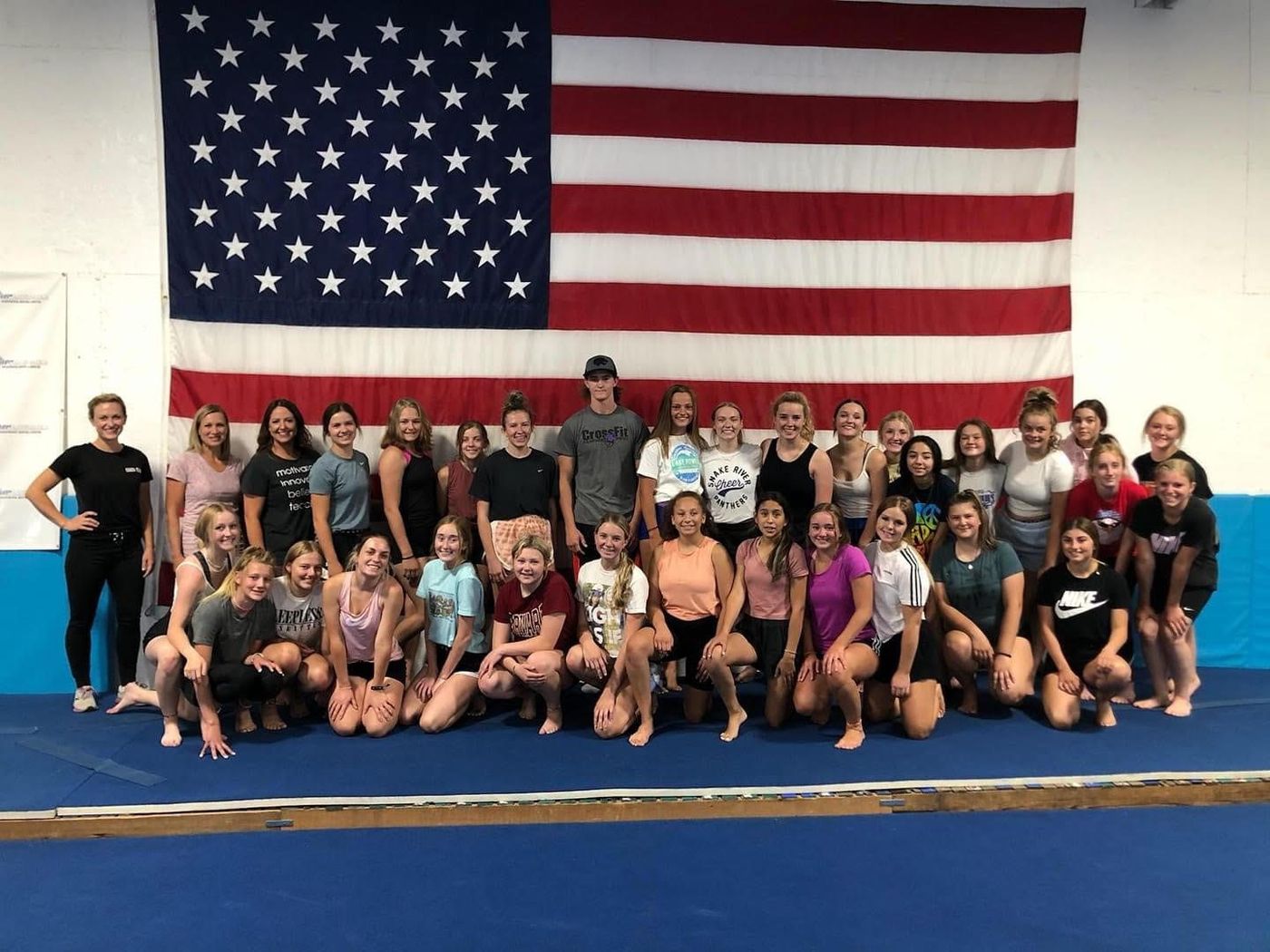 A large group of teen gymnasts and coaches posing in front of an American flag.
