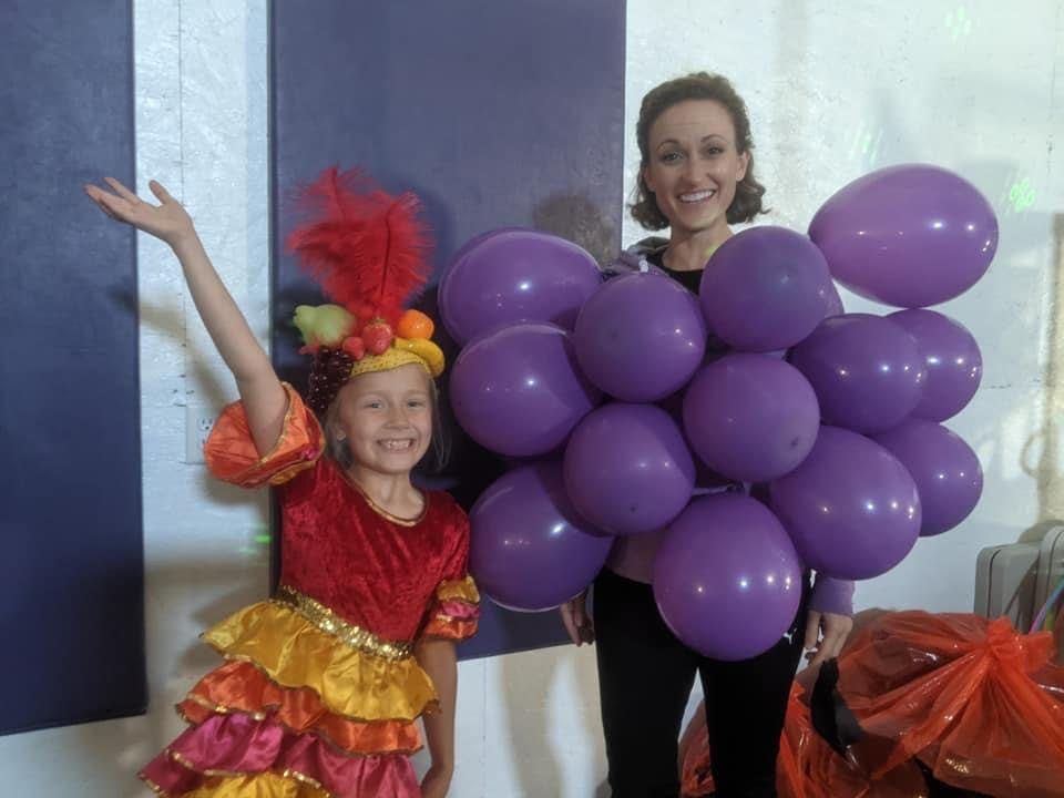 A coach in a grape-cluster balloon costume posing with a girl in a fruit costume at a Halloween event.