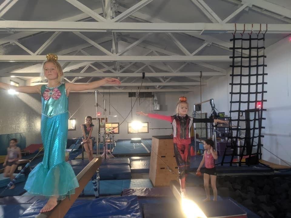Children in costumes practicing balance on beams during a themed gym class.