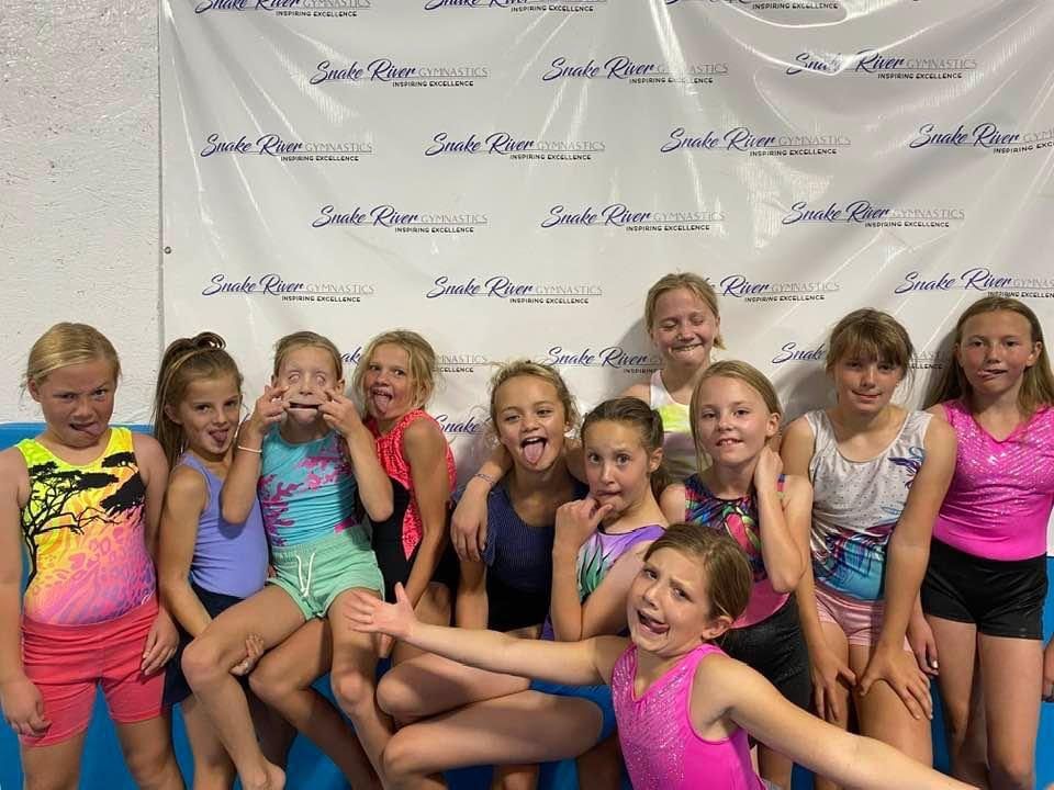 A group of young gymnasts making silly faces in front of a Snake River Gymnastics banner.