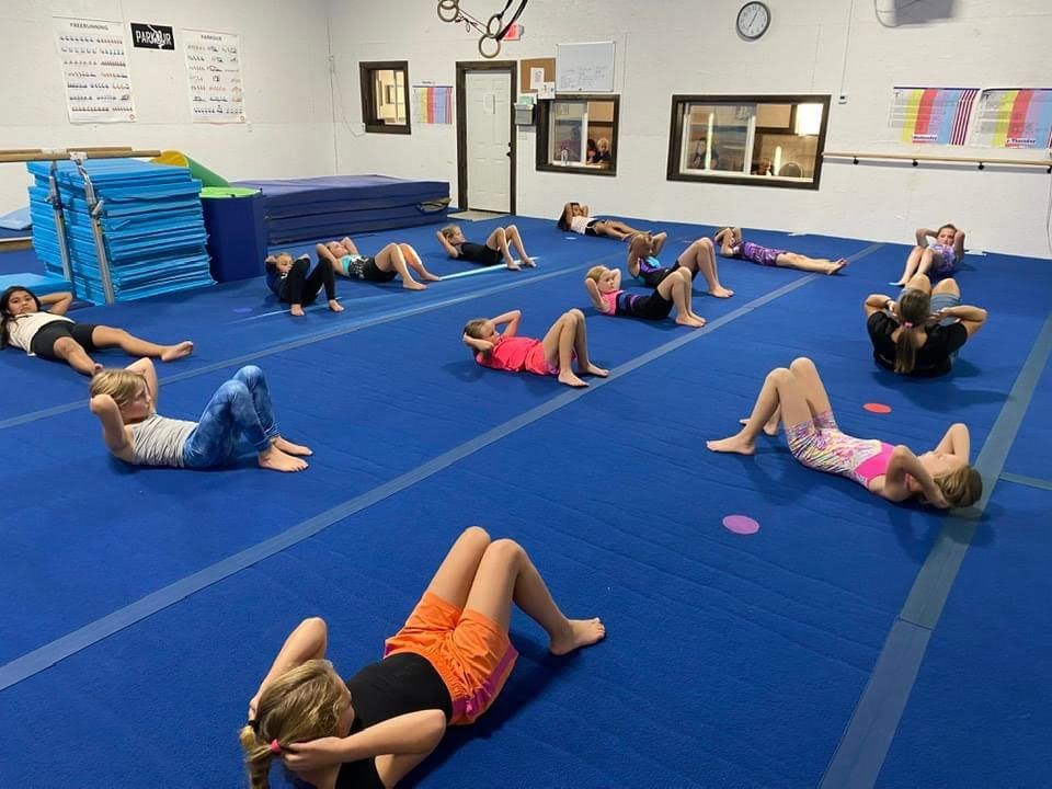 A class of young gymnasts doing sit-ups on blue mats during a conditioning session.