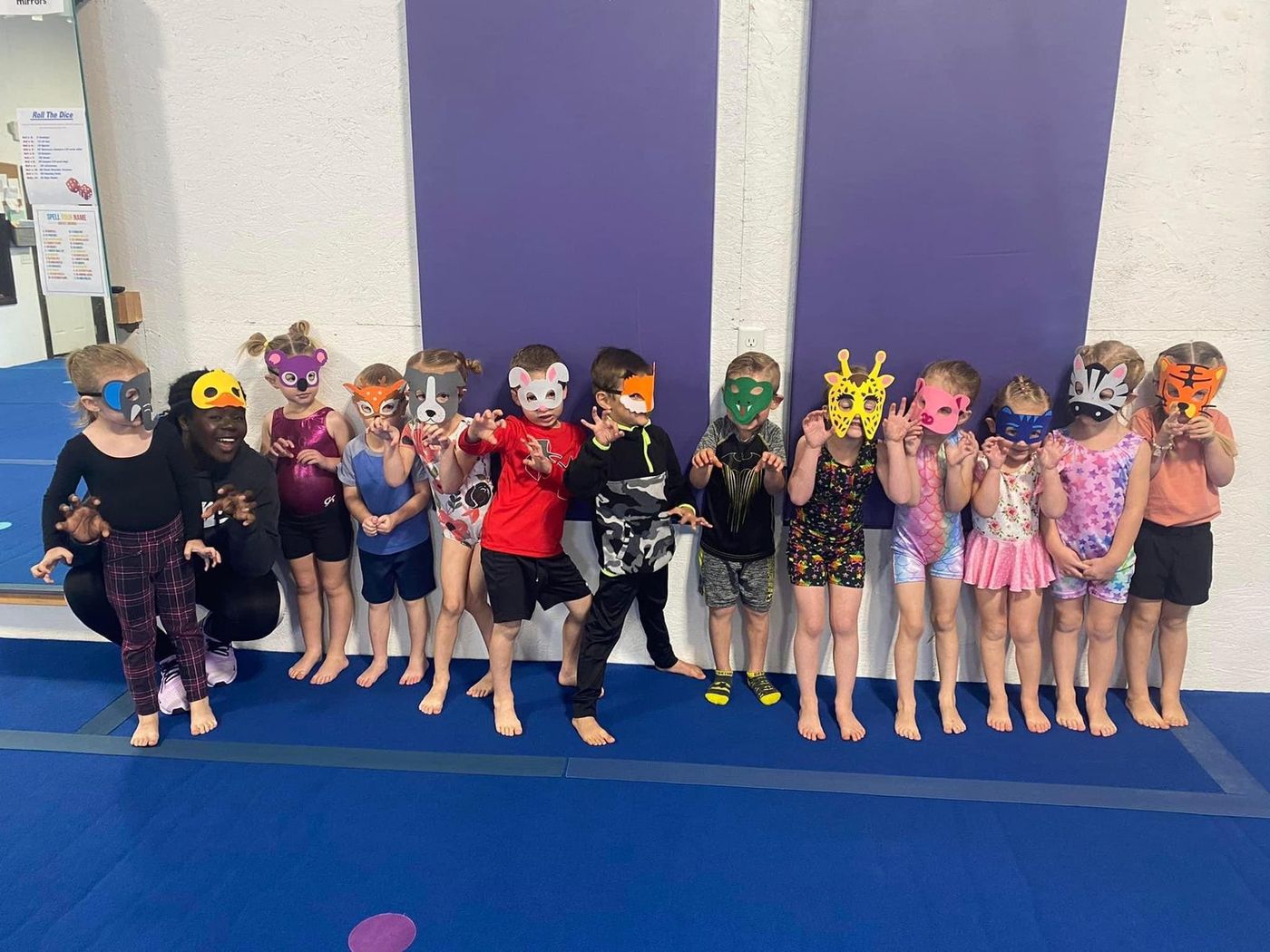 A line of young children wearing colorful animal masks posing in the gym.