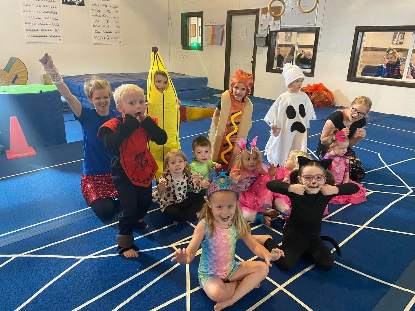 Kids in Halloween costumes posing on a spider-web themed mat during a gym party.