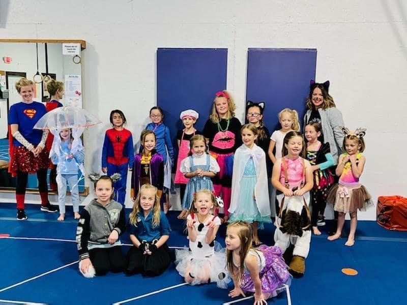 A large group of girls in Halloween costumes posing with two coaches in the gym.