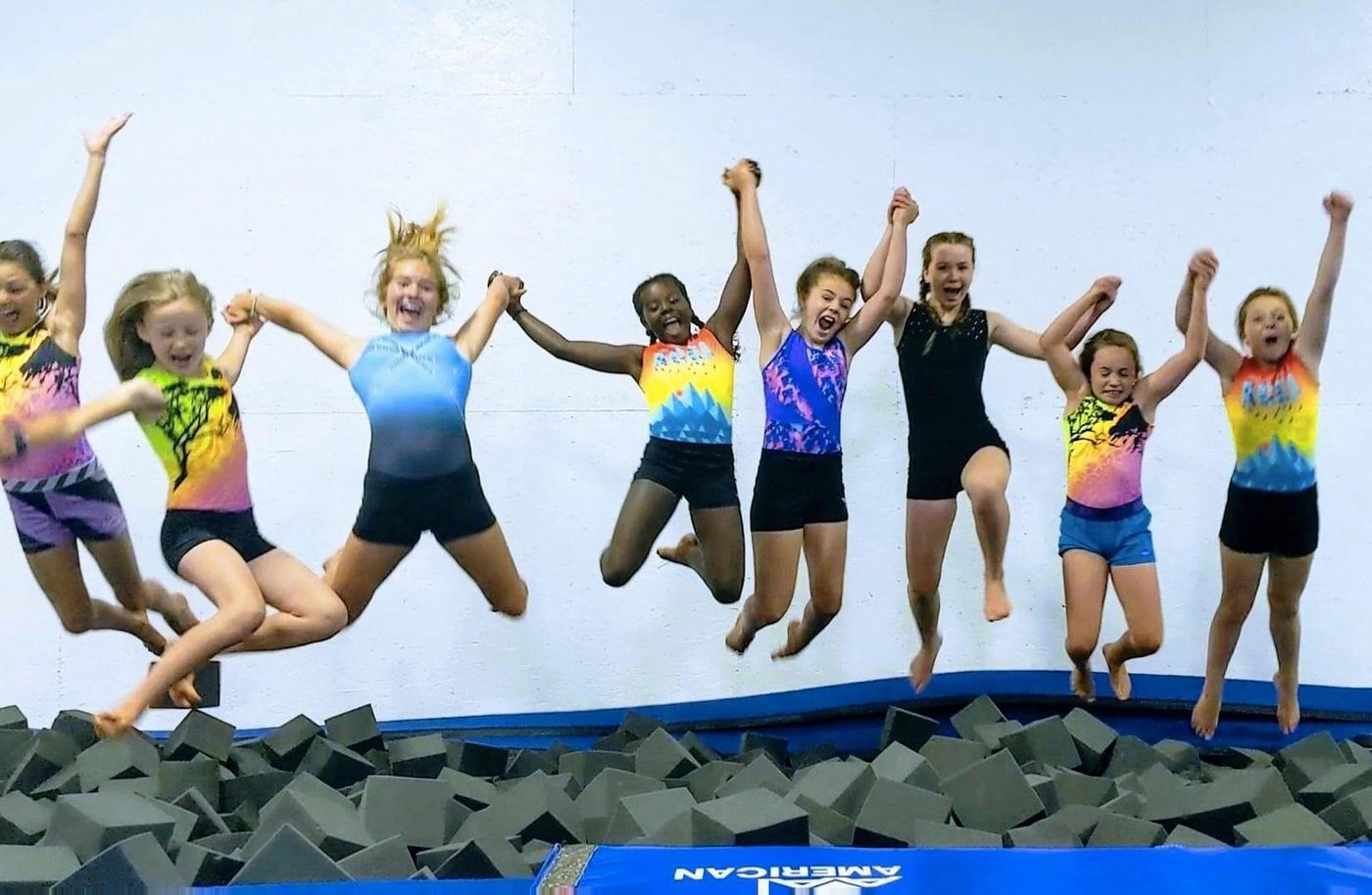 A line of girls jumping in unison into a foam pit during practice.