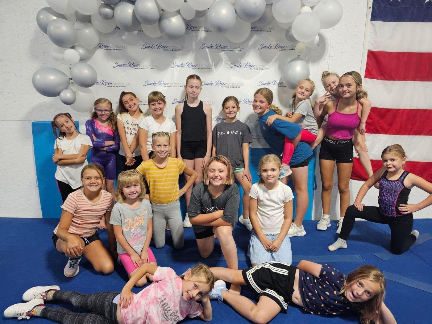 A large group of girls posing together in front of a balloon arch and Snake River Gymnastics backdrop.