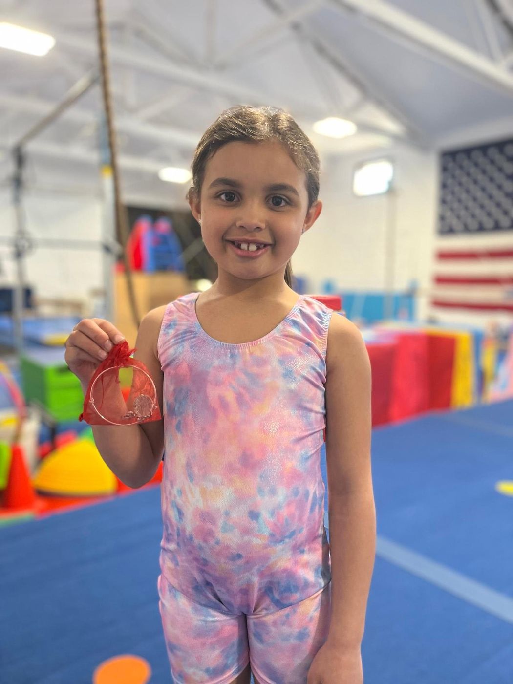 A smiling young gymnast holding a small medal in the gym.