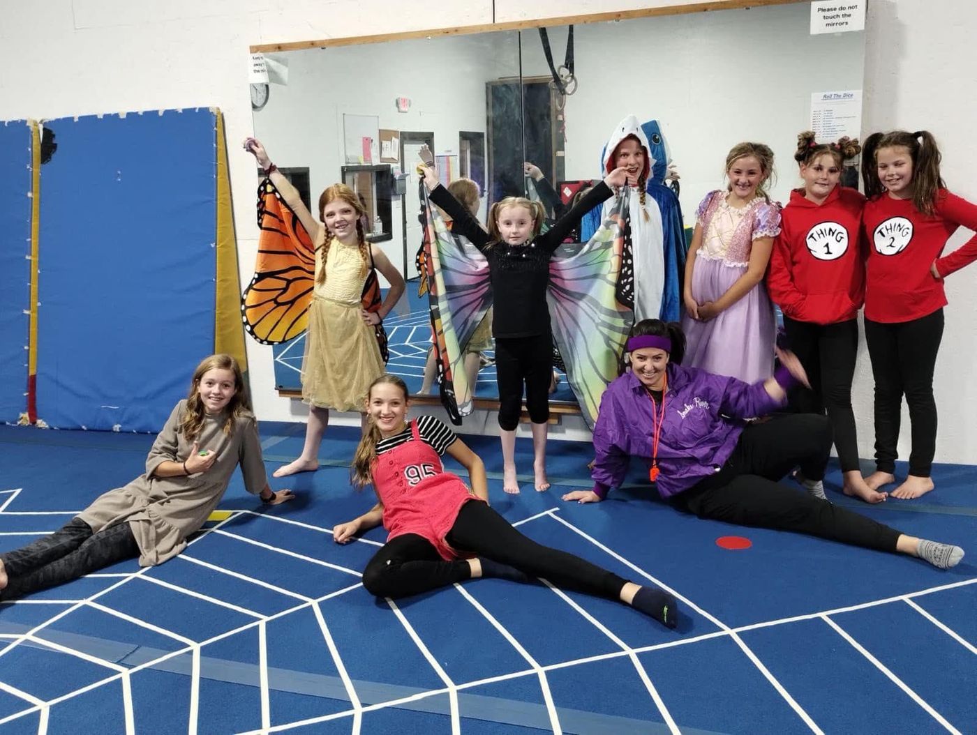 Girls and a coach in Halloween costumes posing on a spider-web mat in the gym.
