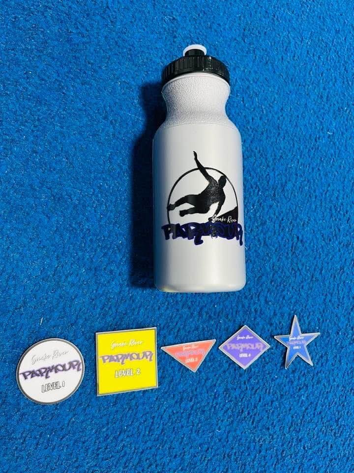 A Snake River Parkour water bottle displayed with the program's level achievement pins on a blue mat.