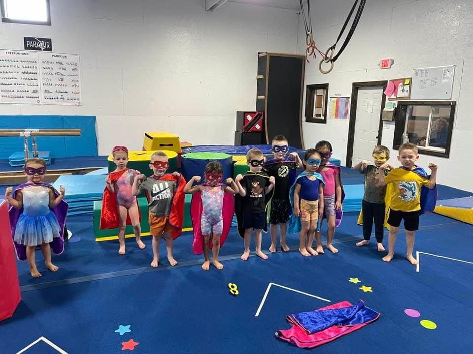 Young children wearing superhero capes and masks lined up during a themed class.