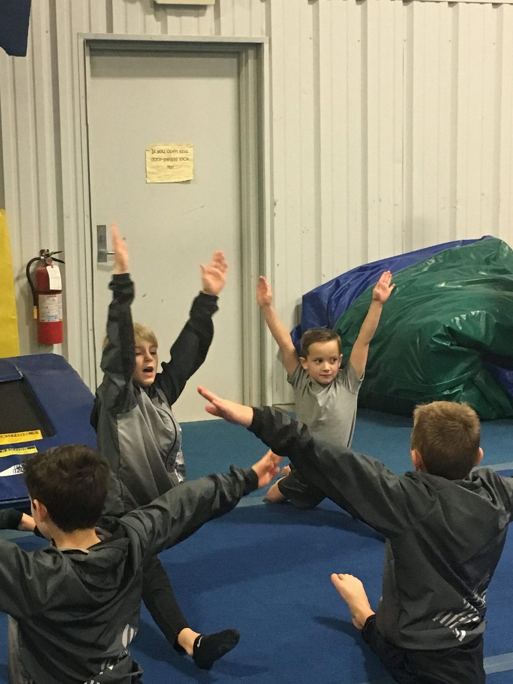 Boys in matching grey jackets stretching and reaching upward during a parkour class.