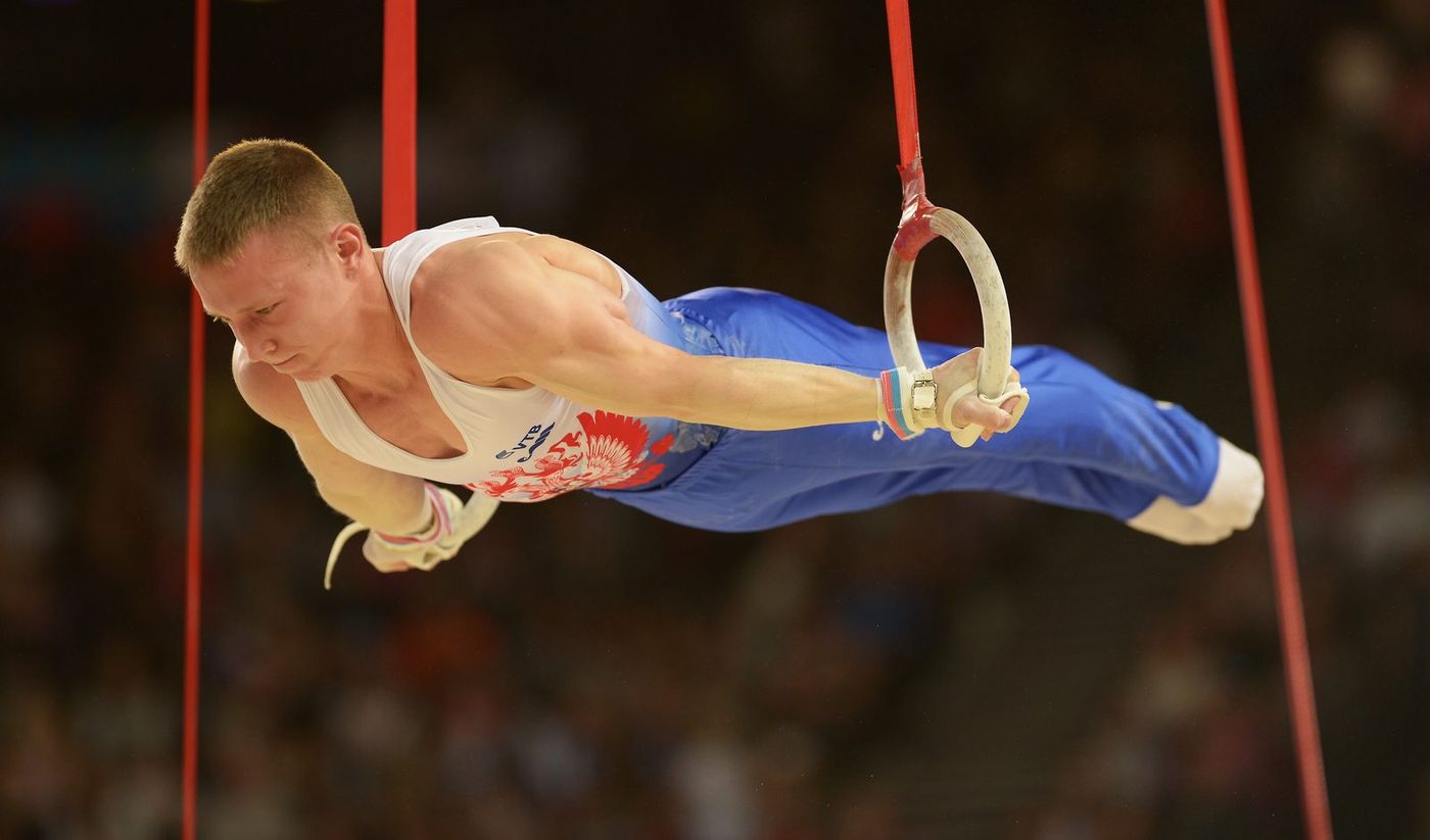 A male gymnast holds a strength position on the still rings during competition.